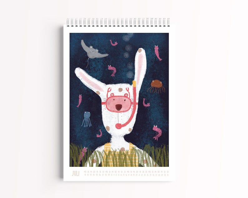 Peut inclure: Un calendrier mural &agrave; spirale pour le mois de juillet illustr&eacute; d'un lapin blanc portant un masque de plong&eacute;e rose et une salopette jaune. Le fond repr&eacute;sente une sc&egrave;ne sous-marine bleu fonc&eacute; avec une raie, des petites crevettes roses et une m&eacute;duse.
