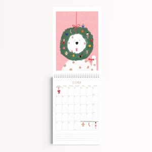 Peut inclure: Un calendrier mural pour le mois de d&eacute;cembre illustrant un chien blanc &agrave; taches brunes portant une grande couronne de No&euml;l verte autour du cou. L'illustration est sur un fond rose &agrave; petits points blancs. La grille du calendrier est en dessous.