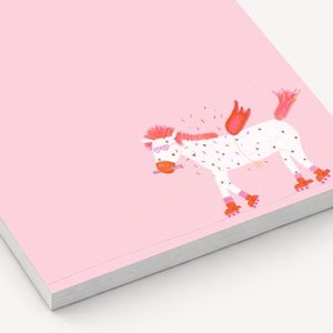 Könnte beinhalten: Ein rosa Notizblock mit einer skurrilen Illustration eines weißen Pferdes mit schwarzen Punkten, Rollschuhen und roten Flügeln. Das Pferd hat eine rosa Mähne und trägt eine Brille. Der Notizblock hat einen weißen Rand.
