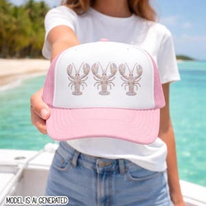May include: A light pink and white trucker hat featuring a graphic print of three identical lobsters arranged horizontally across the front panel. The cap has a solid pink brim and a white mesh back, with a structured front crown design.
