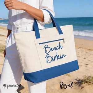 Puede incluir: Un bolso tote grande de lona color crema con una base azul sólido y correas de hombro a juego. La parte frontal cuenta con un bolsillo con cremallera y el texto Beach Birkin impreso en azul oscuro con una fuente cursiva en el centro.