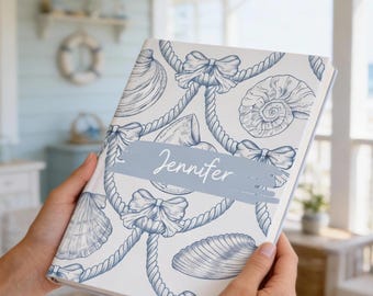 Könnte beinhalten: Ein weißes Notizbuch mit einem blauen nautischen Muster aus Muscheln, Seilen und Schleifen. Ein hellblauer horizontaler Pinselstrich in der Mitte zeigt den Namen Jennifer in weißer Schreibschrift. Der Einband hat ein mattes, detailliertes Design.