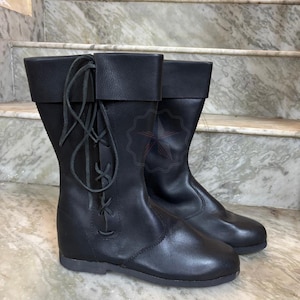 Artisan leather tall boots styled on wooden surface historical vibe.