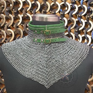Può includere: Un cappuccio di cotta di maglia con colletto e cinturini in pelle verde. Il cappuccio è realizzato con piccoli anelli di metallo ad incastro. Il colletto ha due cinturini con fibbie in ottone. Lo sfondo presenta un motivo di anelli di metallo.
