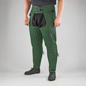 May include: Forest green quilted leg armor featuring a high-waisted design with two black leather buckle straps at the waist. The garment includes black fabric panels at the upper thighs and a circular emblem on the left leg with a star design.