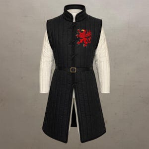 May include: A black quilted sleeveless tunic featuring a high collar, vertical stitching, and a red embroidered griffin emblem on the chest. The garment includes a black waist belt with a gold buckle and is worn over long white quilted sleeves.