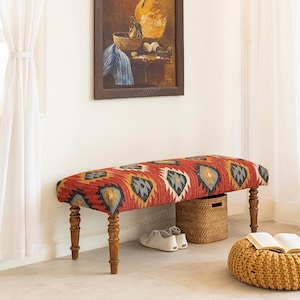 May include: A rectangular bench with a patterned red, yellow, and gray fabric seat. The bench has four wooden legs and is placed in a room with a painting and a woven basket. The bench is approximately 48 inches long.