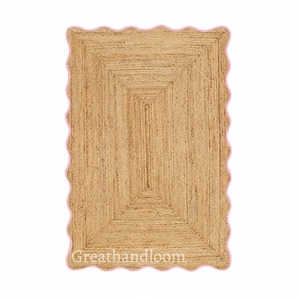 May include: Rectangular jute rug with a light brown center and a pink scalloped border. The rug has a woven texture and a rectangular design within the center. The text "Greathandloom" is visible in the bottom left corner.