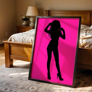 May include: A rectangular framed wall art piece featuring a solid black silhouette of a person standing in a pose with hands near the head, set against a vibrant, solid hot pink background. The frame is thin, black, and surrounds the entire print.