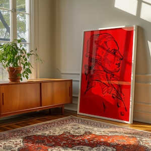May include: A rectangular framed wall art piece featuring a bold, solid red background with a black line-art illustration of a person in profile, wearing a historical-style coat and a tied ponytail, presented in a simple white frame.