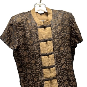 May include: A two-piece set featuring a short-sleeved top and matching shorts. The set is made of a dark brown fabric with a repeating floral pattern. The top has a mandarin collar and beige panels with black frog closures.