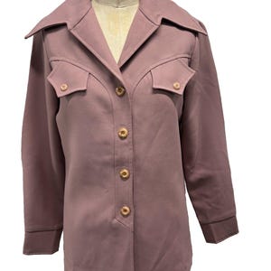 May include: A mauve jacket with a collared neckline and two front pockets. The jacket has long sleeves and wooden-toned buttons. The label on the mannequin reads "WOLF FORM CO. ENGLEWOOD, N.J."