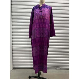 May include: A long, purple dress with a mandarin collar and long sleeves. The dress features a geometric pattern in shades of purple and magenta. It has a button closure at the neckline and a full-length design, displayed on a dress form.
