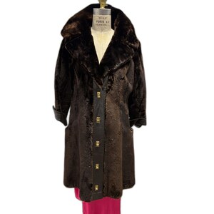 May include: A dark brown vintage coat with a faux fur collar and cuffs. The coat has a long, flowing design with a button-up front and gold-colored buttons. The coat is displayed on a mannequin.