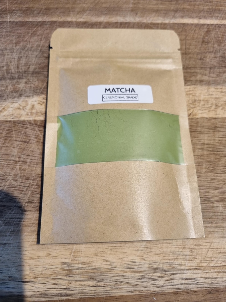 Pu&ograve; includere: Una busta di carta kraft contenente polvere di matcha. La busta ha una finestra trasparente che rivela la vibrante polvere verde. L'etichetta recita "Matcha Ceremonial Grade". La confezione &egrave; sigillata e pronta all'uso.