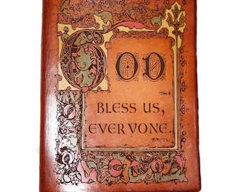 May include: A brown leather-bound journal with a decorative design featuring the word "God" in ornate lettering and the phrase "Bless us, everyone".