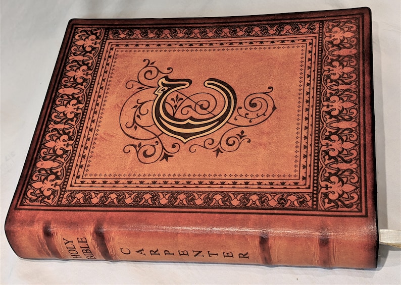 May include: A brown leather-bound Holy Bible with a gold-colored initial "C" and ornate floral designs on the cover. The spine reads "HOLY BIBLE CARPENTER".