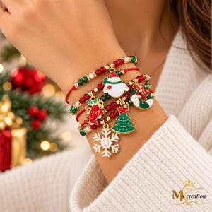 Peut inclure: Un ensemble de bracelets de perles superposés avec des perles rouges, vertes et blanches. Les bracelets comportent des breloques en métal doré en forme de bonhomme de neige, couronne de Noël, cloches, sapin et flocon de neige.