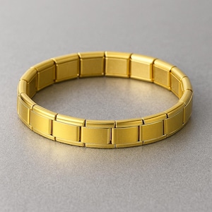 Peut inclure: Un bracelet doré avec un design de maillons rectangulaires. Le bracelet est fait d'un matériau métallique brillant et est présenté sur une surface grise. Le bracelet mesure environ 18 cm de circonférence.