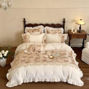 May include: A bed with a floral patterned comforter and matching pillow shams. The bedding features a cream-colored base with a floral design in shades of brown and beige. The comforter has a lace trim and ruffled edges.