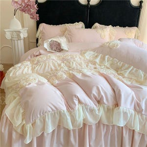Può includere: Un lussuoso set di biancheria da letto rosa e crema con bordi a balze e dettagli floreali. Il set include un copripiumino, cuscini e una gonna da letto. Il copripiumino e i cuscini presentano delicate decorazioni a forma di rosa.
