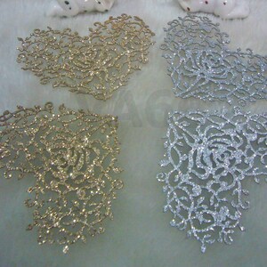 May include: Four heart-shaped glitter embellishments in gold and silver. The embellishments are made of a delicate, lacy material with a floral design.