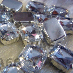 May include: A close-up of a group of clear glass rhinestones with silver settings. The rhinestones are various shapes and sizes, and they are arranged in a random pattern.