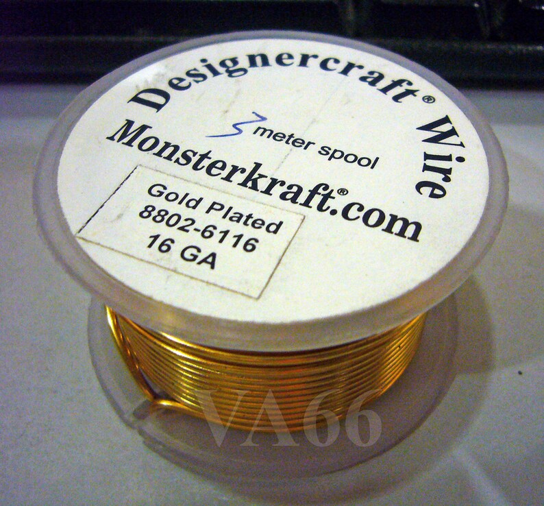 K&ouml;nnte beinhalten: Eine Spule mit vergoldetem Draht, beschriftet mit "Designercraft Wire", "Monsterkraft.com", "Gold Plated 8802-6116 16 GA" und "1 Meter Spule".
