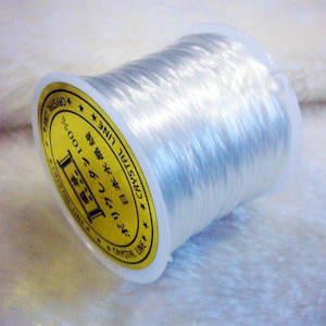 May include: A spool of clear elastic thread with a gold label that reads "CRYSTAL LINE 日本水晶线 ボリウレタン 100%" in Japanese and English.