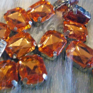 Pode incluir: Um close-up de um grupo de strass de vidro laranja facetados com engastes prateados. Os strass estão dispostos em um padrão aleatório.