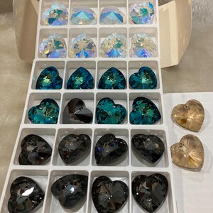 May include: A clear plastic container with 20 heart-shaped crystal beads. The beads are in various colors, including clear, teal, and black.