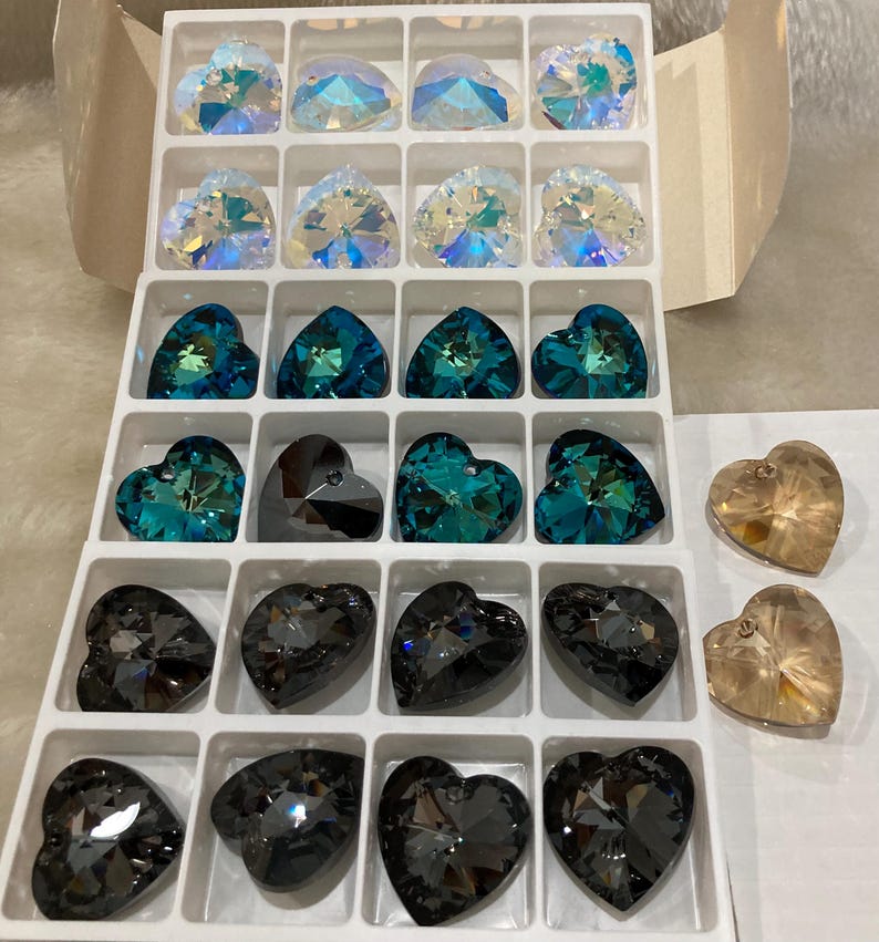 May include: A clear plastic container with 20 heart-shaped crystal beads. The beads are in various colors, including clear, teal, and black.