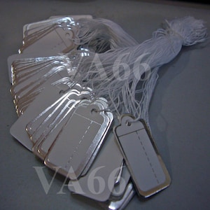 May include: A stack of silver-colored price tags with white labels and a white string attached. The tags are rectangular with rounded corners and have a hole at the top for attaching the string.