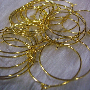 May include: A pile of gold-colored hoop earrings. The hoops are all different sizes and are arranged in a random pattern.