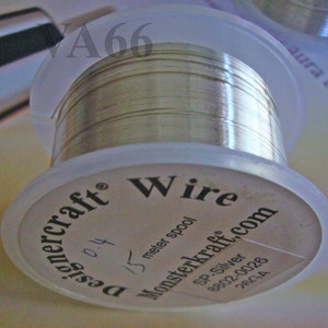 May include: A spool of silver wire, labeled "DesignerCraft Wire." The spool is clear plastic, with the wire tightly wound. The label includes "Monsterkraft.com," "SP-Silver," and "26GA."