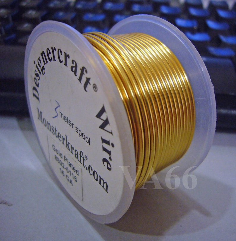 K&ouml;nnte beinhalten: Eine Spule mit goldplattiertem Draht, 3 Meter lang, beschriftet mit "Designercraft Wire" und "Monsterkraft.com". Die Spule ist mit "Gold Plated 18 GA" beschriftet und befindet sich auf einem wei&szlig;en Hintergrund.