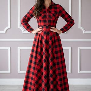 May include: A floor-length long-sleeve dress featuring a red and black buffalo plaid pattern, a collared neckline, a button-down front, and two chest pockets. The garment has a fitted bodice and a full, flowing skirt that reaches the floor.