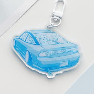 May include: A light blue car-shaped keychain with a white clasp. The car illustration features cartoon fish inside. The license plate reads "FRNT06".