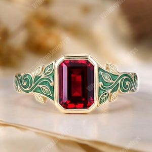 Op de afbeelding: Een gouden ring met een rechthoekige, smaragdgeslepen rode edelsteen in het midden. De ringband is versierd met groene emaille details in een rank- en bladpatroon dat zich vanaf de centrale zetting langs beide zijden uitstrekt.