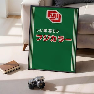 Puede incluir: Un póster verde enmarcado con rayas verticales blancas y texto japonés. El póster presenta un logotipo rojo y blanco en la parte superior. Una cámara vintage y un libro marrón están frente al póster.