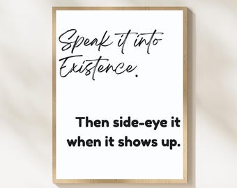 May include: A framed print with the text "Speak it into Existence. Then side-eye it when it shows up." The text is in black script on a white background, framed in a light brown wooden frame. The background is a light beige color.