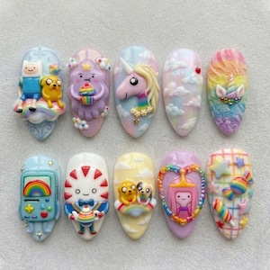 May include: A set of ten artificial nails, each uniquely designed with colorful, cartoon-themed art. Designs include a unicorn, cloudscapes, and characters from Adventure Time. The nails are oval-shaped and feature a variety of colors and textures.
