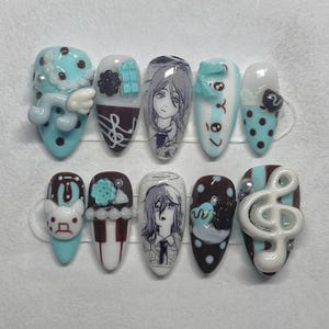 May include: A collection of ten artificial nails with diverse designs. The nails showcase cartoon characters, musical notes, and decorative elements in blue, brown, white, and red. Some nails have 3D embellishments.