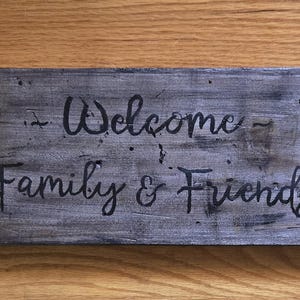 手描きの「家族と友人を歓迎します」 - 素朴な農家風の壁装飾。