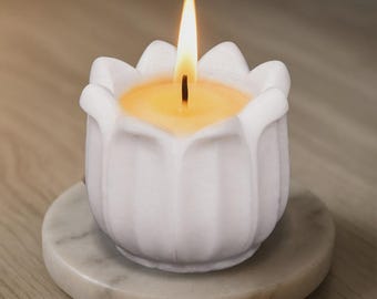 May include: A lit white candle in a tulip-shaped holder, resting on a marble coaster. The candle's flame is bright yellow, and the wax inside the holder is a warm yellow. The holder has a detailed, petal-like design.