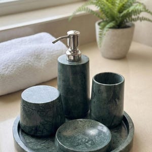 Op de afbeelding: Een groene marmeren badkamerset bestaande uit een zeepdispenser, een beker, een kleine pot met deksel, een zeepbakje en een rond dienblad. De set heeft een natuurlijk steenpatroon.
