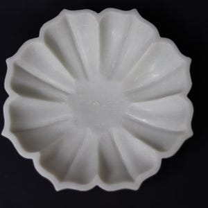 May include: A white, flower-shaped decorative bowl with a scalloped edge. The bowl has a textured surface and is set against a black background. The bowl's design resembles a blooming flower, suitable for decorative purposes.