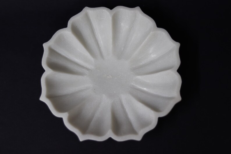 May include: A white, flower-shaped decorative bowl with a scalloped edge. The bowl has a textured surface and is set against a black background. The bowl's design resembles a blooming flower, suitable for decorative purposes.