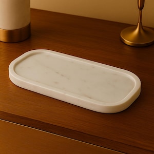 May include: A rectangular white marble tray with rounded corners. The tray is set on a dark wood surface. The marble has subtle grey veining. The tray is approximately 30 cm long and 13 cm wide.