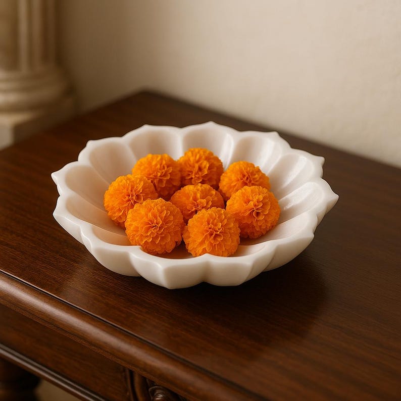 May include: A white, scalloped-edge bowl filled with vibrant orange marigold flowers. The bowl sits on a dark wooden surface, creating a contrast with the bright flowers. The flowers are in full bloom, showcasing their intricate petal structure.